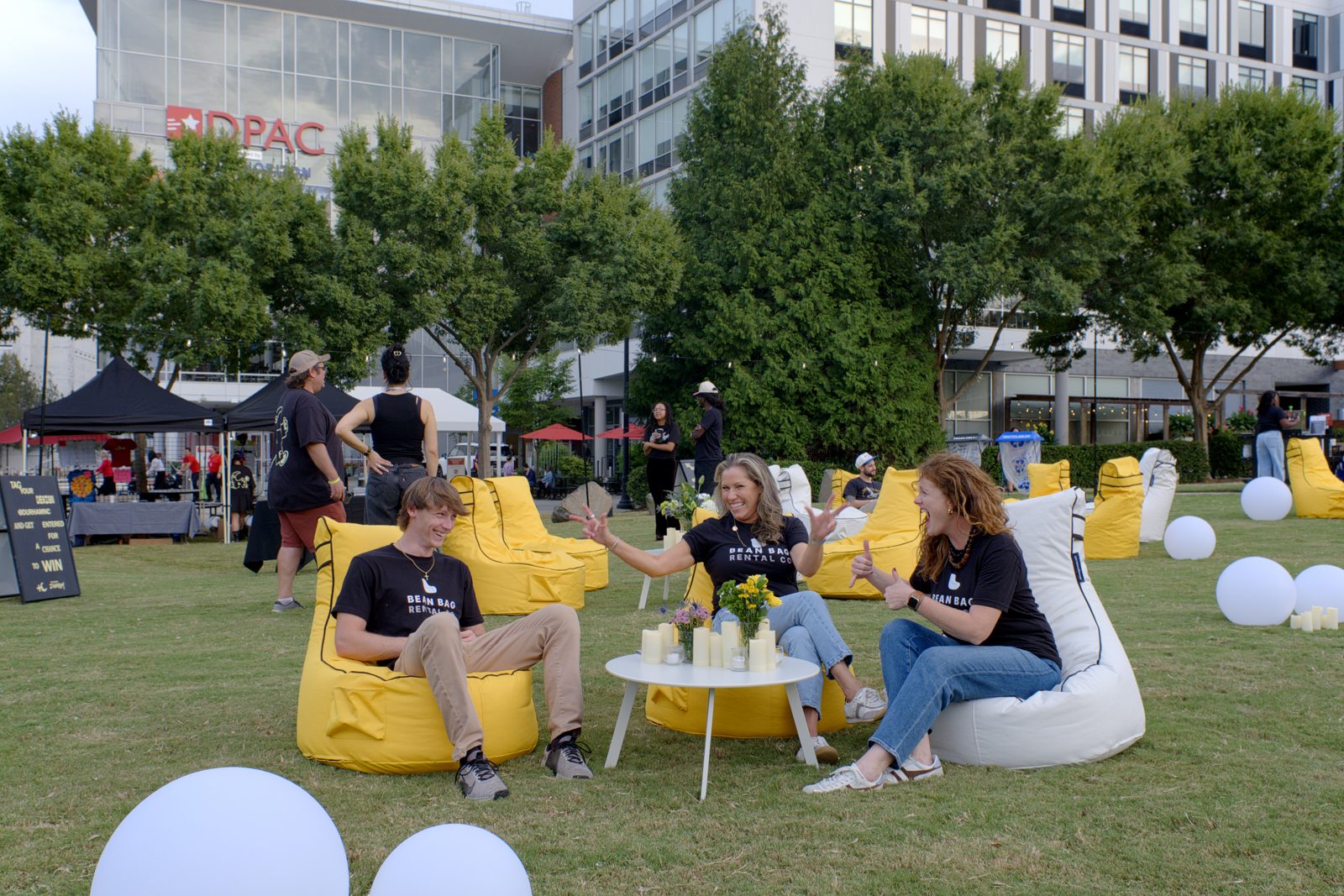 Guests relaxing in a pod of yellow and white high-back bean bag chairs around a coffee table on a city lawn